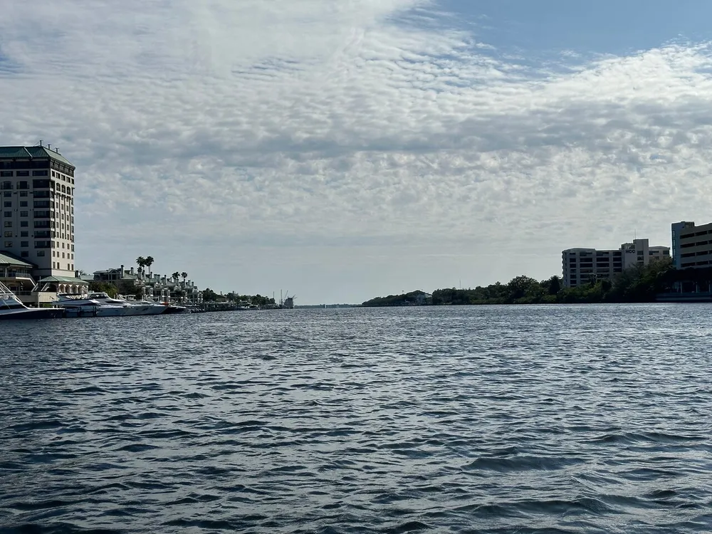 The image shows a waterfront view with buildings on the left a clear horizon and a partly cloudy sky above a broad expanse of water