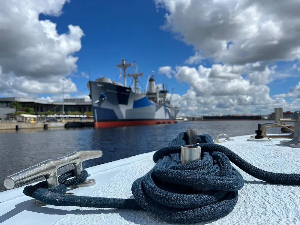 A coiled rope on the deck of a boat with a blurred cargo ship in the background under a partly cloudy sky