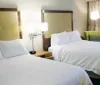 This image shows a tidy hotel room with two made-up beds bedside lamps and a green accent chair