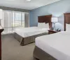 The image shows a neatly arranged hotel room with two double beds a television and a large window with a view