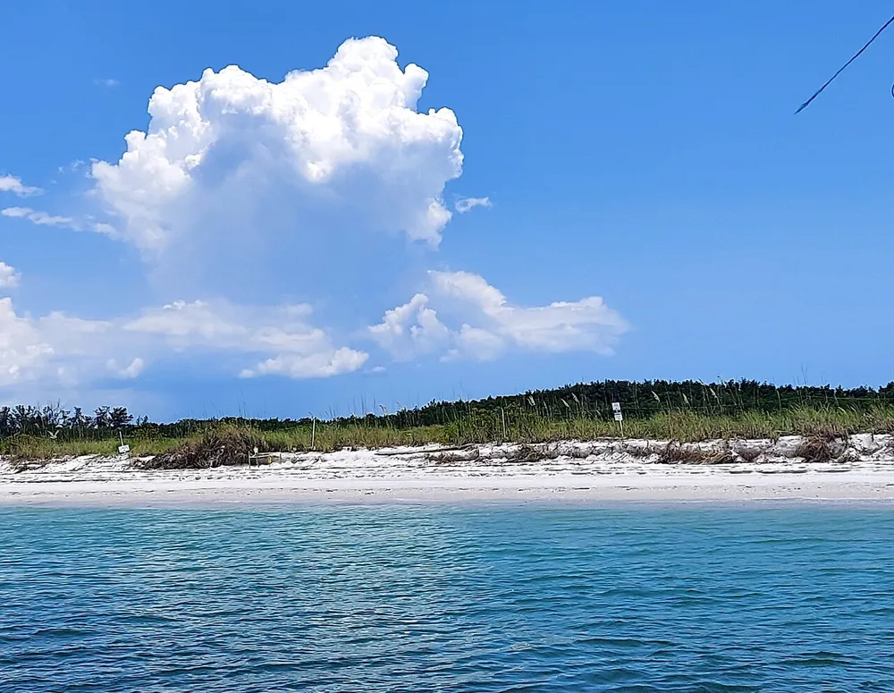 This image captures a serene beach scene with a towering cumulus cloud above the coastline under a bright blue sky