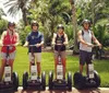 Four individuals are standing outdoors on Segways wearing helmets and casual summer clothing with tropical foliage in the background