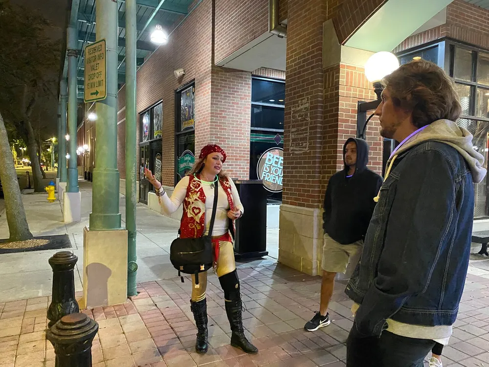 A person dressed in a pirate costume is animatedly talking to two others on a city sidewalk at night