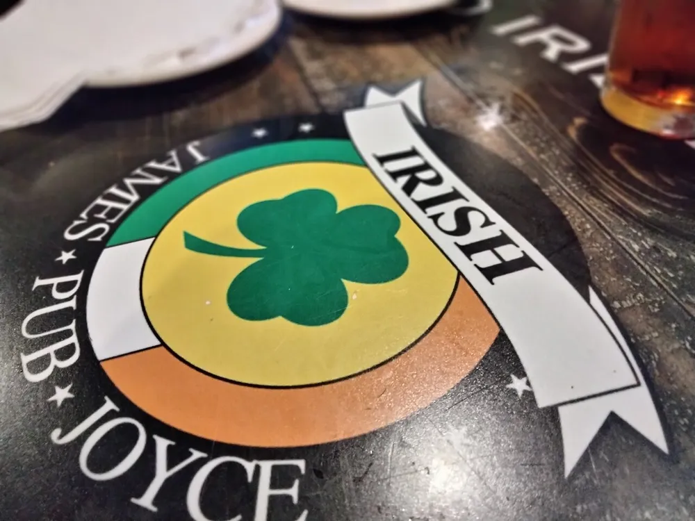 A close-up image of a tabletop design at an Irish pub featuring the name Joyce a green shamrock and a partial view of a plate and a glass with a beverage