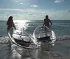 Two people are smiling and paddling in a clear kayak amongst mangrove trees