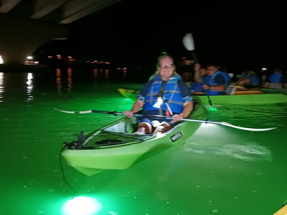 A person is kayaking at night with illuminated green water around them likely from underwater lights