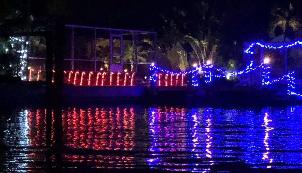 The image shows a lakeside view at night illuminated by red and blue decorative lights which are reflecting beautifully on the waters surface