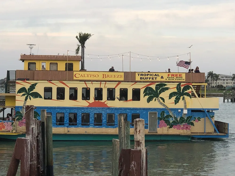 A brightly colored boat named Calypso Breeze is docked offering a tropical buffet and free rum punch with people visible on its upper deck