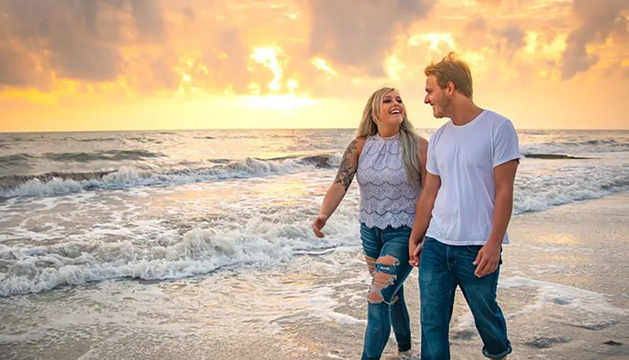 A happy couple is walking along the beach, enjoying a beautiful sunset over the ocean.
