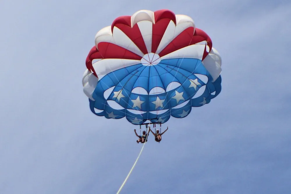 Two people are enjoying a parasailing experience with a parachute adorned in a red white and blue design with stars