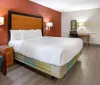This is a well-lit tidy hotel room featuring a large bed with white bedding a teal armchair a work desk and contemporary decor
