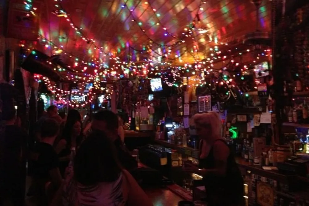 The image shows a bustling bar scene with colorful string lights creating a vibrant cozy atmosphere