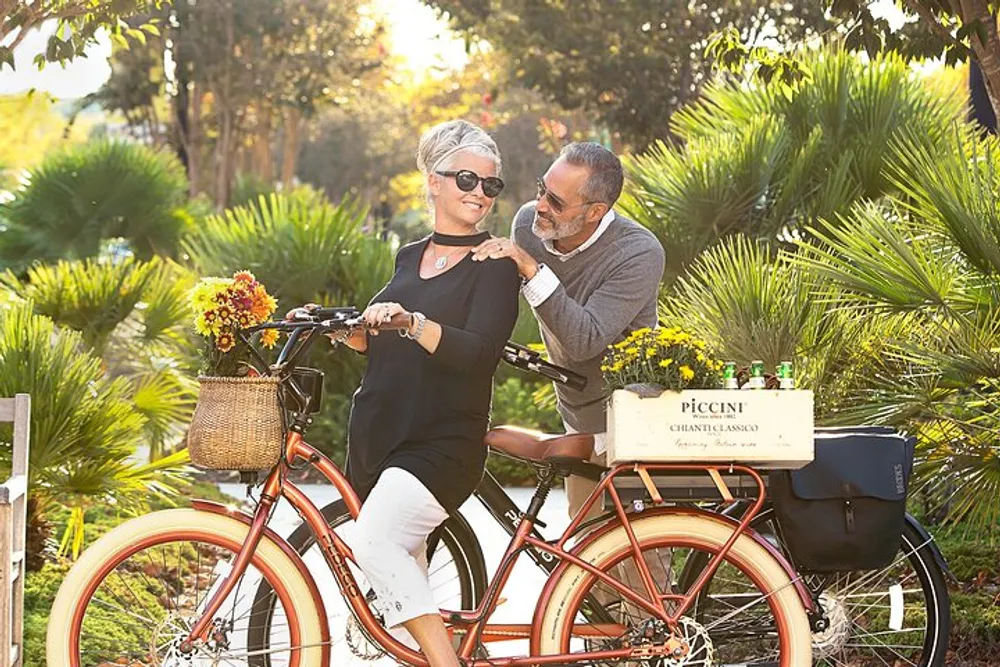 A happy couple shares an affectionate moment on a bicycle surrounded by lush greenery in a sunlit park
