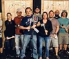 A group of cheerful people wearing matching Axe Throwing Tampa shirts pose with axes in front of a wooden target wall at an axe-throwing venue