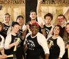 A group of cheerful people wearing matching Axe Throwing Tampa shirts pose with axes in front of a wooden target wall at an axe-throwing venue