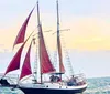 A sailboat with red sails is navigating the sea under a clear blue sky with several people visible on deck