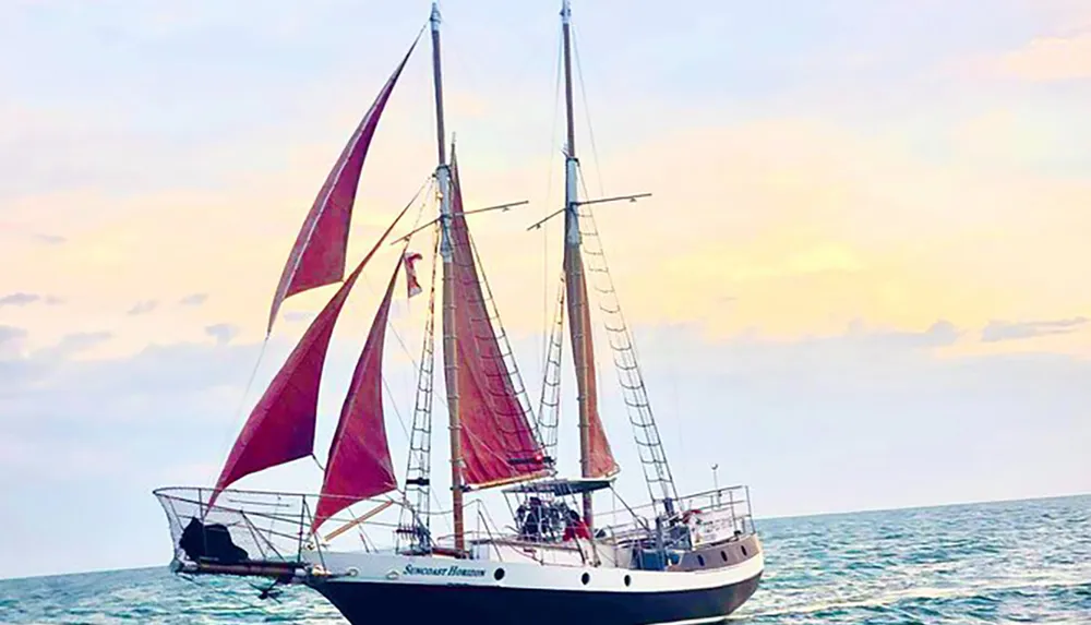 A sailboat with red sails is sailing on the sea against a soft pastel sky