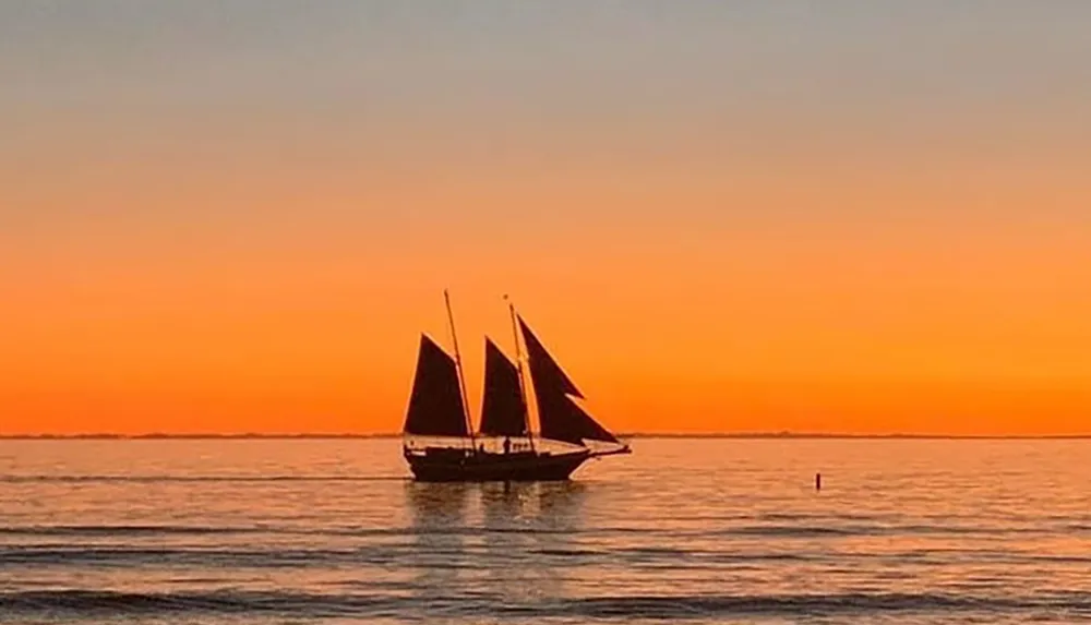 A sailboat is silhouetted against a vibrant orange sunset on the water