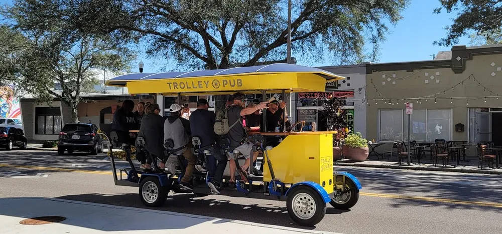 A group of people enjoy pedaling together on a yellow multi-passenger Trolley Pub vehicle on a sunny street