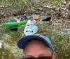 A group of people are kayaking in a mangrove forest with the forefront showing a selfie of a man wearing sunglasses and a baseball cap