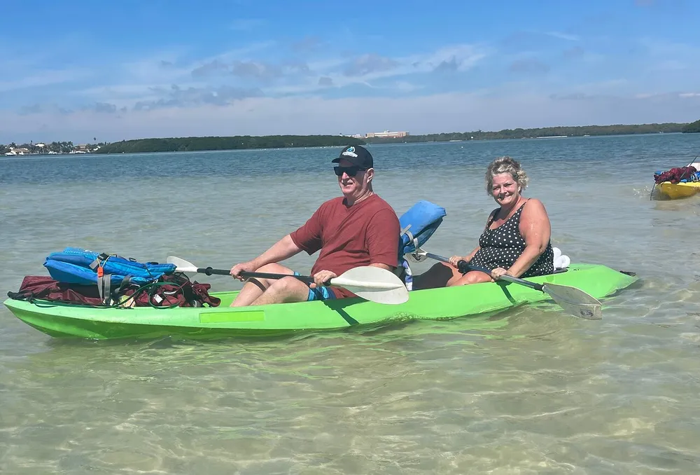 Two people are smiling and enjoying a sunny day while kayaking in clear shallow waters