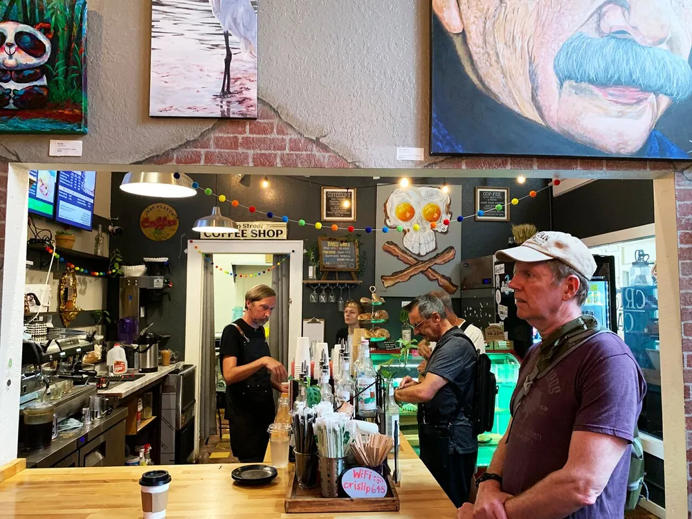 Patrons await their orders in a vibrant coffee shop adorned with colorful artwork and eclectic decor