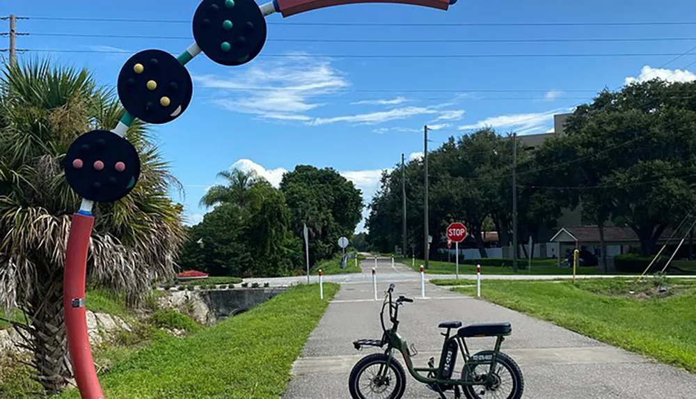 This image shows a whimsical street view featuring oversized playful sculptures of pick-up sticks and buttons with a bright green bike parked in the foreground