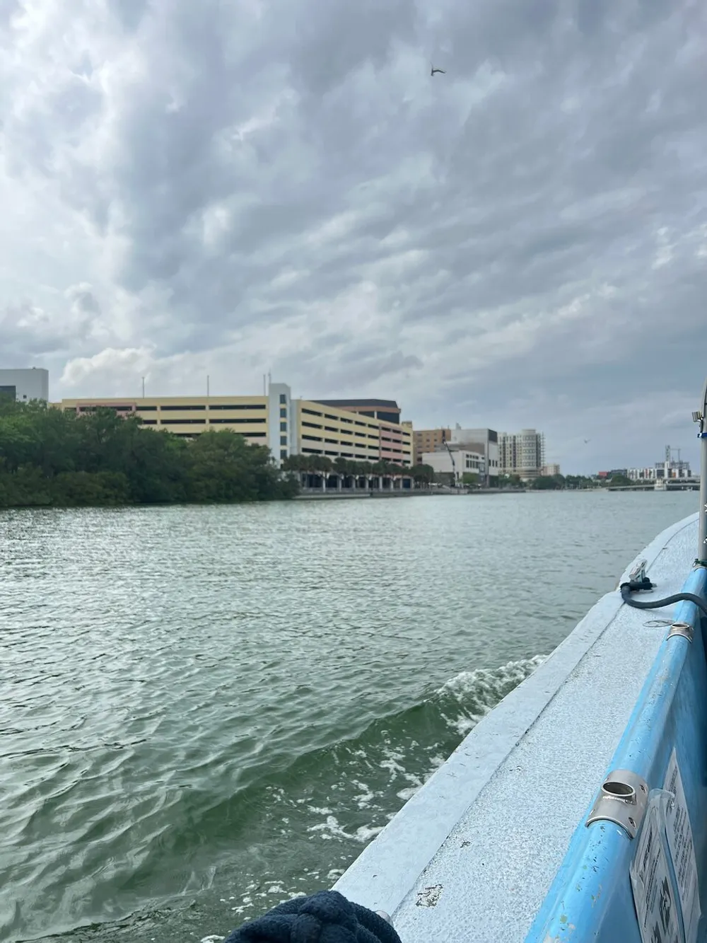 The image features a view from a boat showing choppy water in the foreground and a city skyline under a cloudy sky in the background
