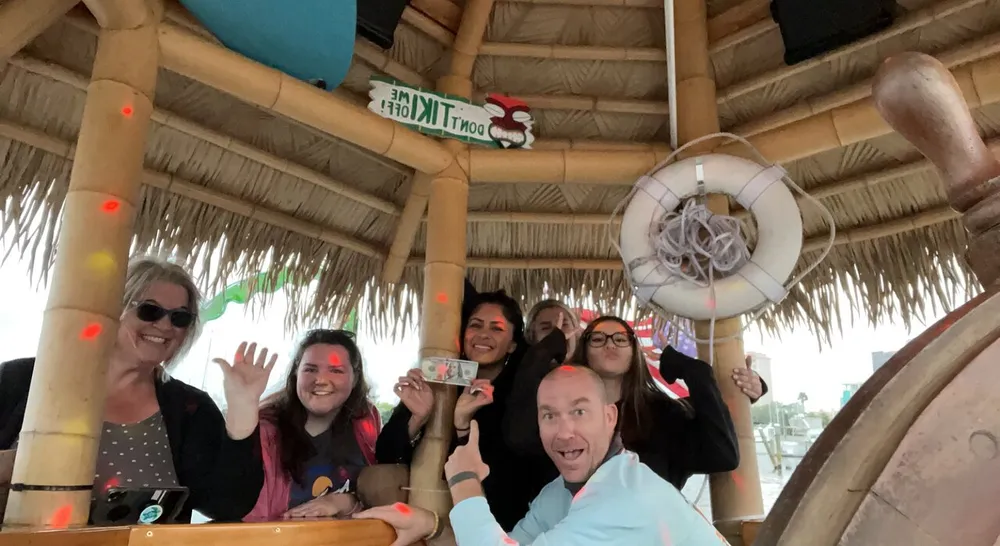 A group of cheerful people posing and waving inside a tiki bar-themed setting