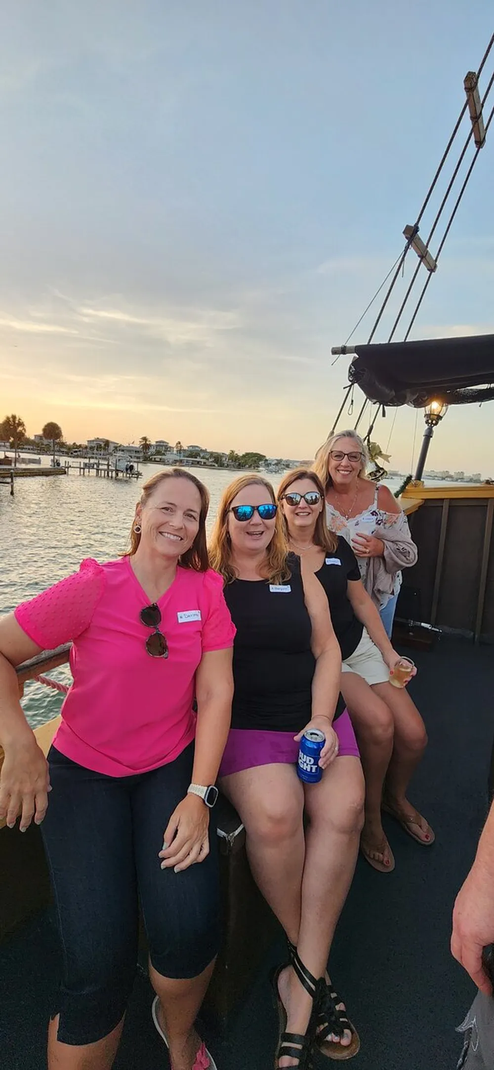 Four people are smiling for a photo while enjoying a boat ride during the sunset with calm waters and docks visible in the background