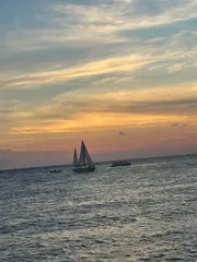 The image shows a sailboat on the ocean at sunset with colorful skies and scattered clouds above.