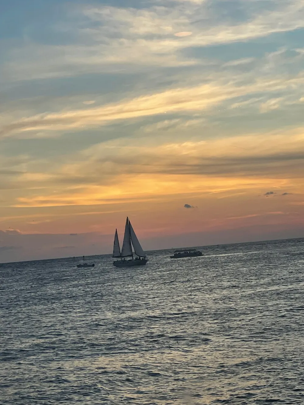 The image shows a sailboat on the ocean at sunset with colorful skies and scattered clouds above