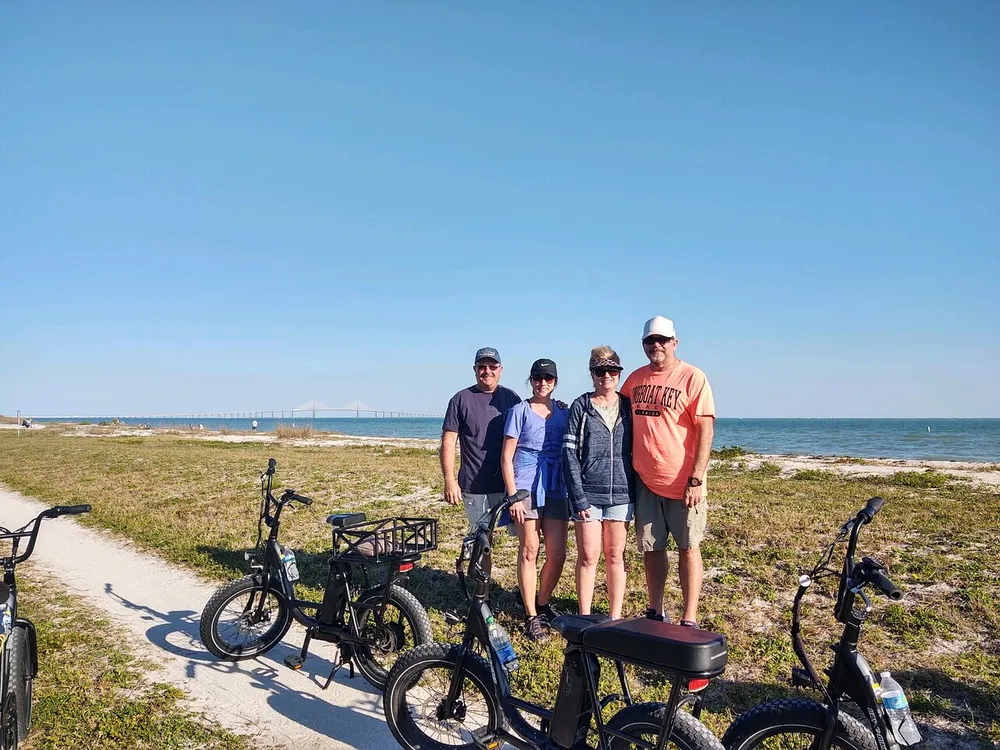 Four people and a couple of bicycles are posed against a scenic coastal backdrop with a bridge in the distance