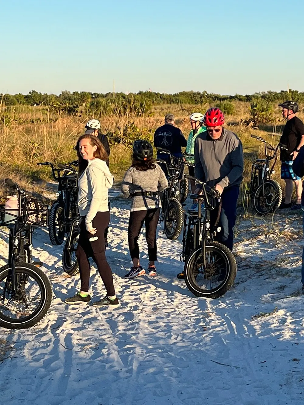 A group of people with bicycles are enjoying their time on a sandy trail under the bright sunlight