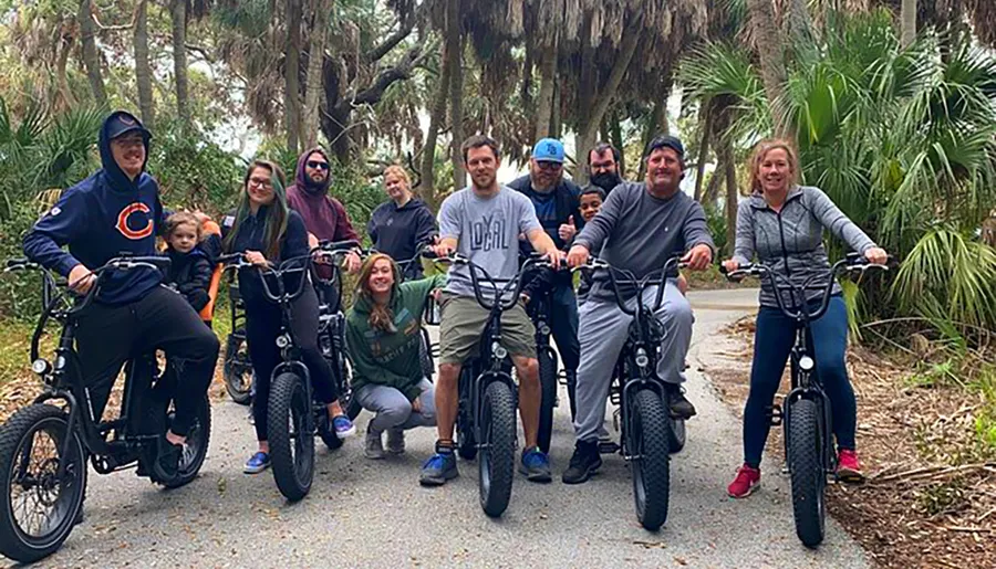 A group of happy people posing with their bicycles on a tree-lined path.