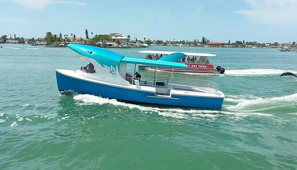 A boat designed to look like a shark is cruising on the water with passengers onboard while a dolphin is jumping in the background