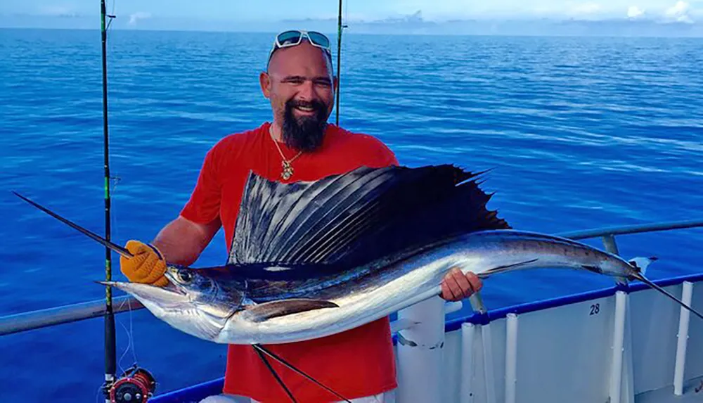 A smiling man is holding a large sailfish on a boat with the ocean in the background