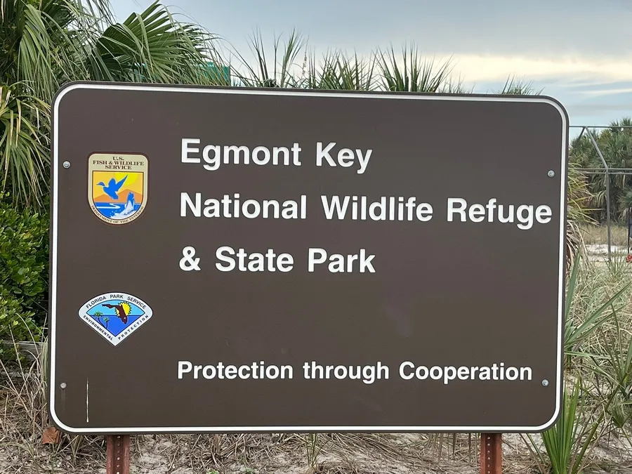 The image shows a sign for Egmont Key National Wildlife Refuge & State Park with the motto Protection through Cooperation, featuring logos of the U.S. Fish & Wildlife Service and the Florida Park Service.