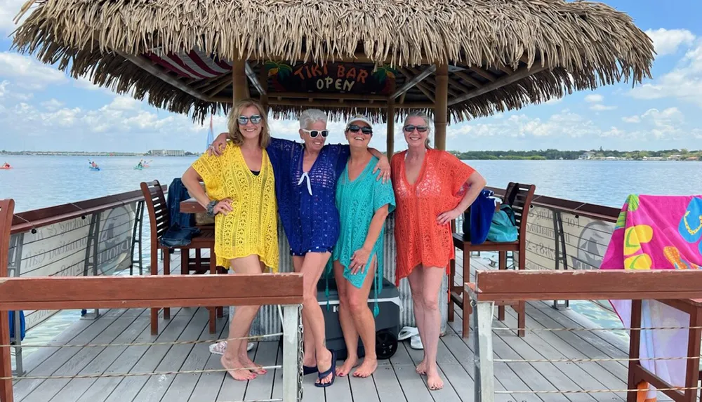 Four people are smiling for the camera while standing together at a lakeside tiki bar on a sunny day