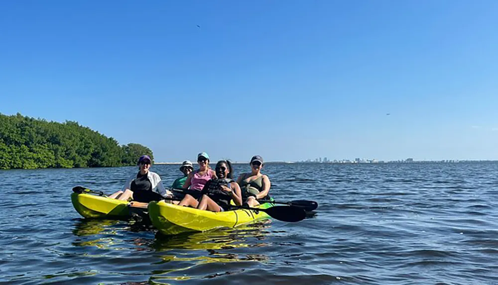 Five individuals are enjoying a sunny day out on the water in a tandem kayak with a coastline visible in the distance