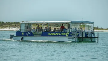 A ferry boat filled with passengers is cruising near a shoreline.