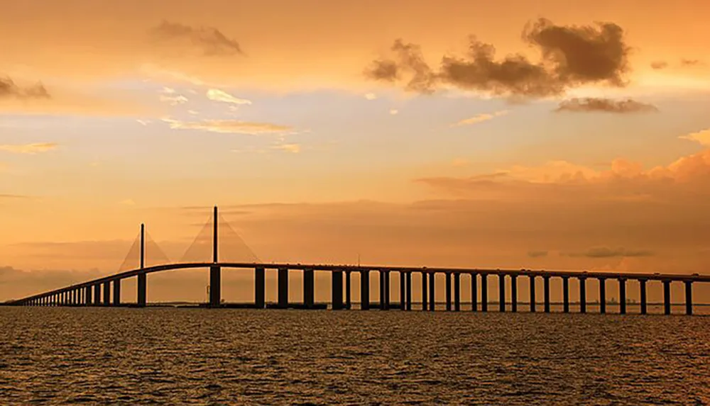 A long bridge spans across a body of water under a golden sky at sunset
