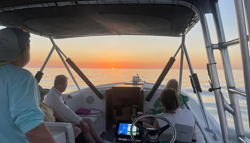 A group of people on a boat are enjoying a serene sunset over a calm sea