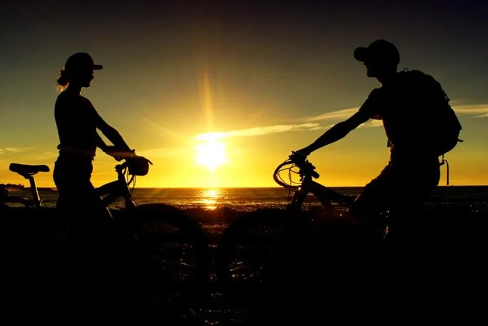 Two cyclists are silhouetted against a beautiful sunset on the beach