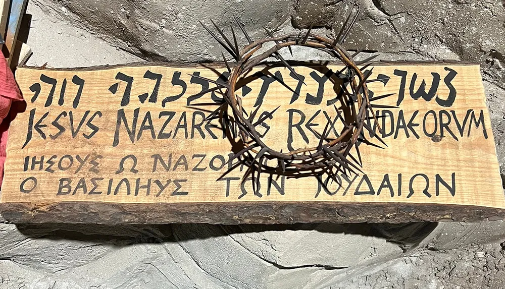 The image shows a wooden sign with the inscription Jesus of Nazareth King of the Jews in three languages Hebrew Latin and Greek accompanied by a crown of thorns reminiscent of the titulus crucis associated with the crucifixion of Jesus Christ