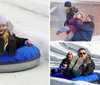 A joyful child slides down a snowy hill on a blue inflatable snow tube wearing a winter jacket and a knitted hat