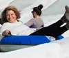 A joyful child slides down a snowy hill on a blue inflatable snow tube wearing a winter jacket and a knitted hat