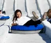 A joyful child slides down a snowy hill on a blue inflatable snow tube wearing a winter jacket and a knitted hat