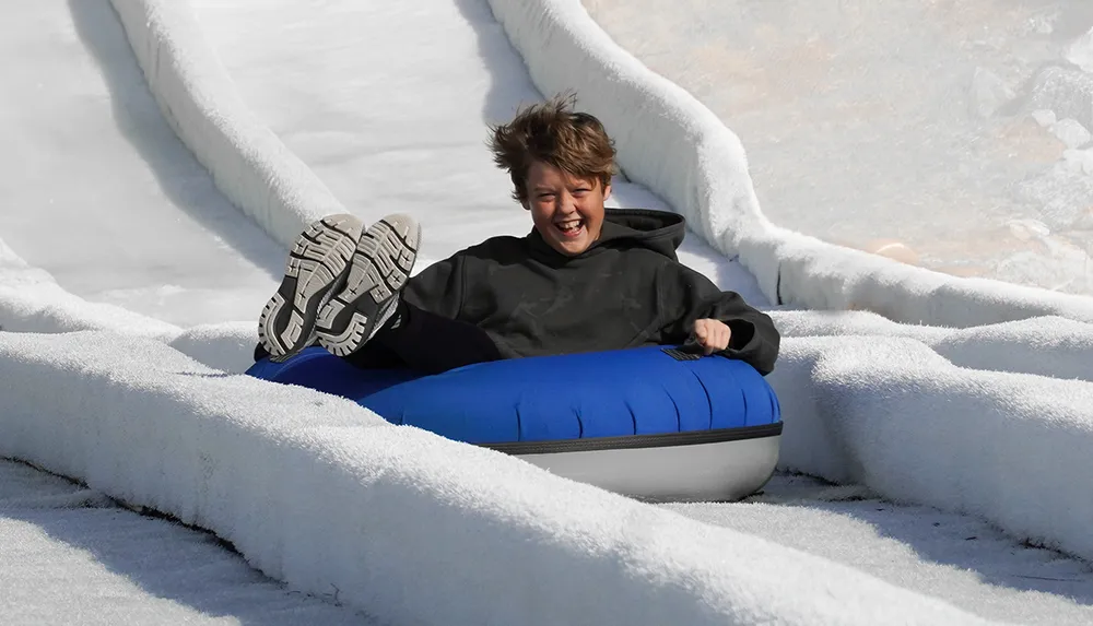 A person is joyfully sliding down a snowy hill on a blue inner tube