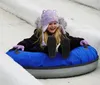 A joyful child slides down a snowy hill on a blue inflatable snow tube wearing a winter jacket and a knitted hat